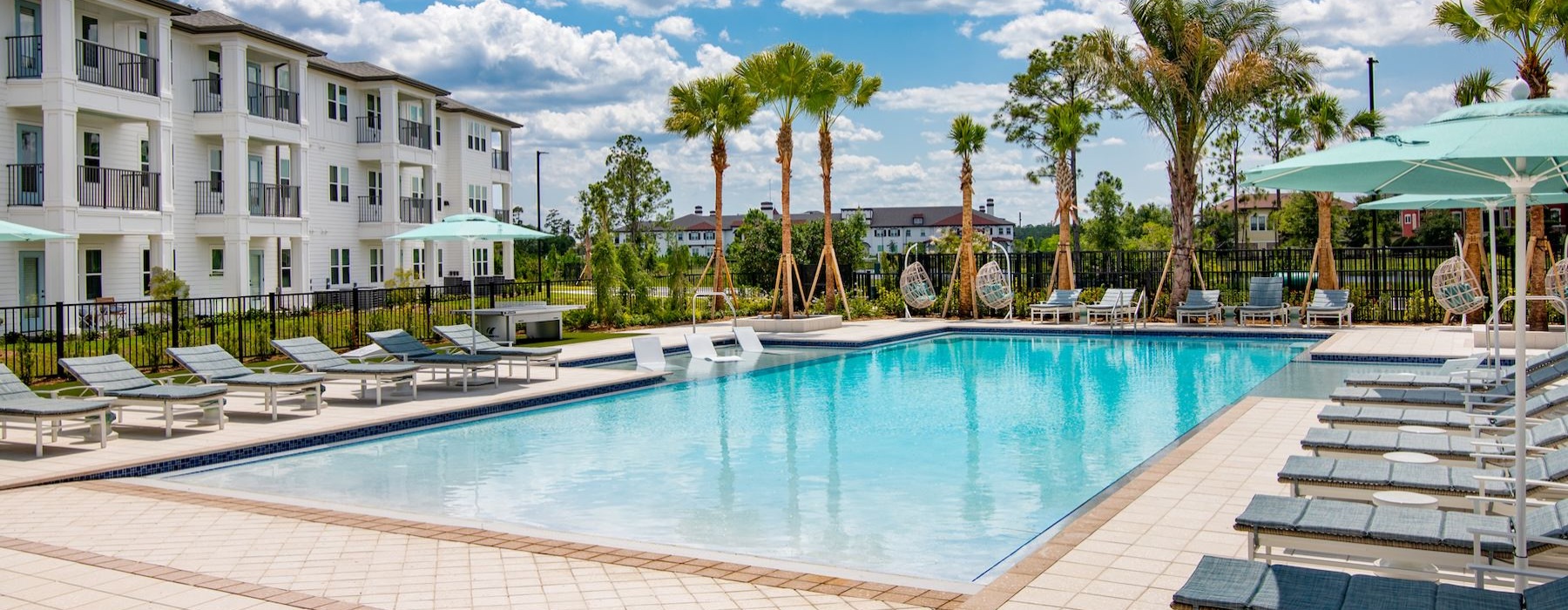 a swimming pool with lounge chairs and umbrellas by a building